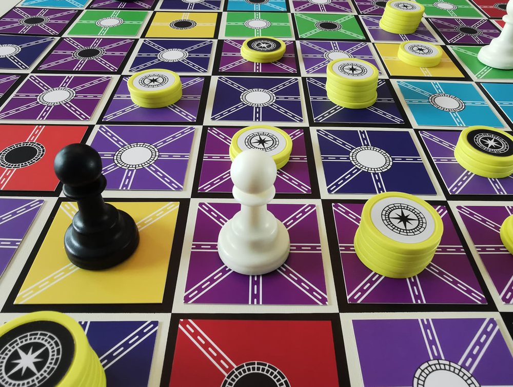A close view of the physical game: coloured road tiles, two pawns and stacks of yellow gold